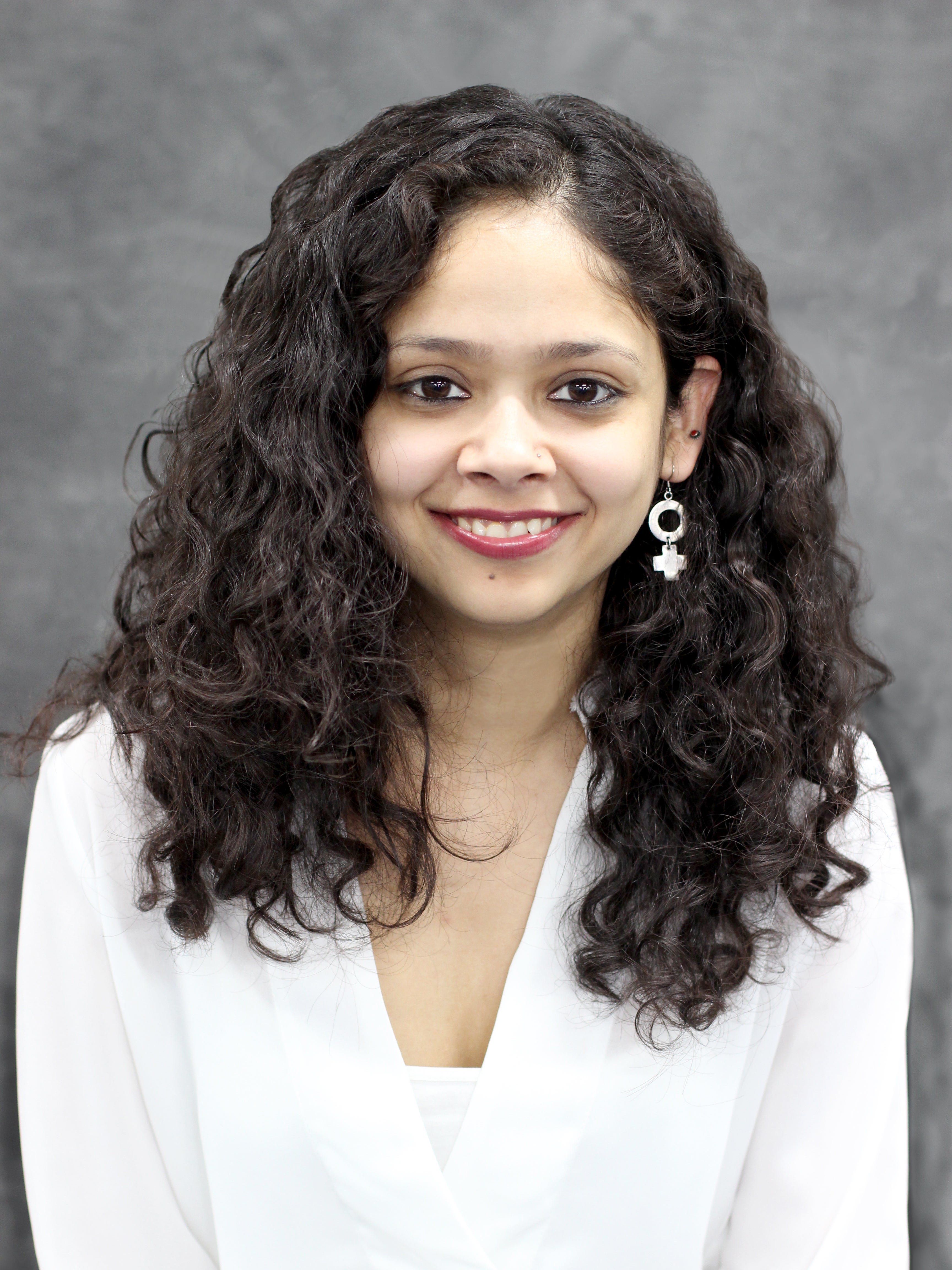 Women with long brown curly hair in a white shirt in front of a grey background